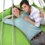 A man and woman laying on a green hammock.