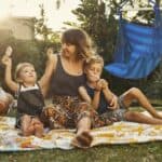 A woman and two children sitting on a blanket in a backyard.