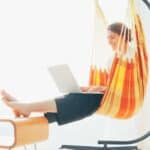 A woman using a laptop in a hammock chair.