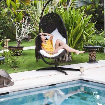A woman is sitting in a hanging chair next to a pool.
