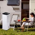 A woman sitting in a chair next to a portable air conditioner.