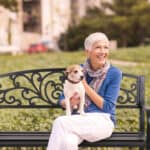 An older woman sitting on a park bench with her dog.