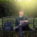 A young man sitting on a bench with a tablet computer.