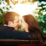 A man and woman are sitting on a bench in a park.