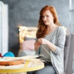 A woman is sitting at a table and knitting.