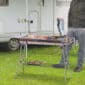 A man standing in front of a camper with a bbq grill.