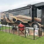 A large rv parked in a grassy area with a man and a dog.