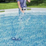 Person cleaning a swimming pool with a manual vacuum cleaner.