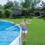 Woman cleaning a backyard swimming pool with a telescopic pole.