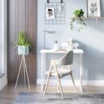 A modern minimalist home office setup with a white desk, a grey chair, plants, and decorative wall hangings.