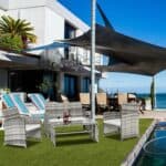 Modern beachfront house with poolside loungers and outdoor furniture.