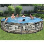 Group of people enjoying themselves in an above-ground swimming pool with a stone-patterned exterior.