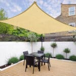 A beige sunshade canopy over an outdoor dining area with a table and chairs on a wooden deck.