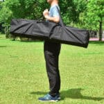 A man carrying a large black bag in a park.