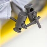 Close-up of a pair of black cylindrical cord locks on a gray garment against a blurred yellow background.