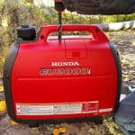 Portable red honda eu2000i generator placed outdoors on the ground.