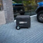 A portable generator with a protective cover parked on a driveway.