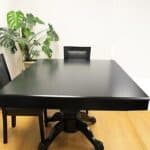 An empty black conference table with one chair in a room with a potted plant in the corner.