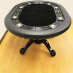 Round black poker table with cup holders on a wooden floor.