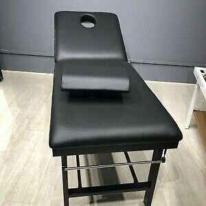 Examination table with black upholstery and a headrest in a clinical setting.