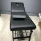 Examination table with black upholstery and a headrest in a clinical setting.