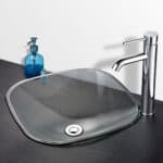 A glass bathroom sink with a faucet and soap dispenser.