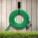 A green garden hose hanging on a wooden fence.