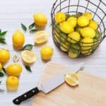 A basket of lemons on a cutting board with a knife.