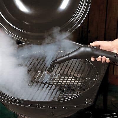 A person is using a steamer to clean a bbq grill.