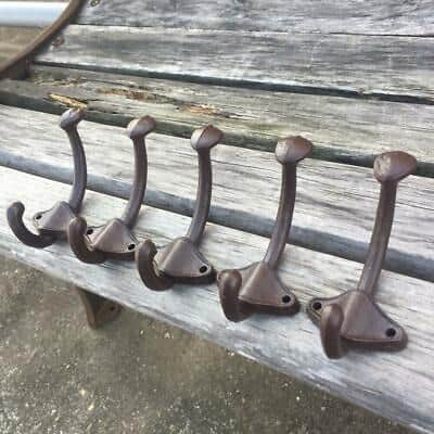 Five metal coat hooks on a wooden bench.