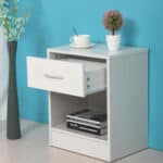 A white nightstand with a book and a vase.