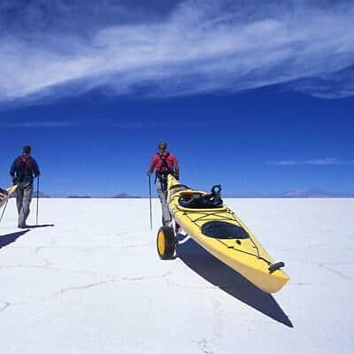 Two people walking with kayaks on the salt flats.