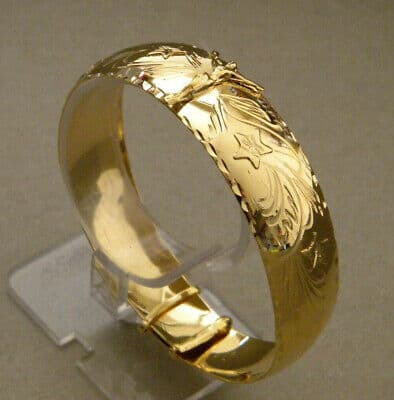 A gold plated bangle bracelet on a stand.