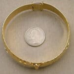 A gold bracelet with a coin next to it.