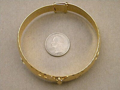 A gold bracelet with a coin next to it.