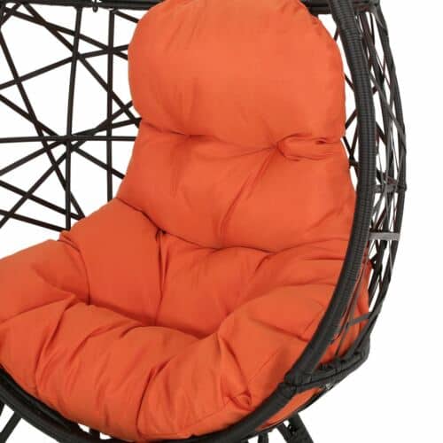 A hanging chair with an orange cushion.