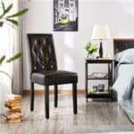 A black dining chair in front of a bed in a bedroom.