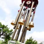 Close-up of a set of wind chimes with cylindrical metal tubes and wooden parts on a blurred natural background.