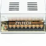 An electronic device, specifically a zyltech branded unit with multiple connection terminals visible through a clear plastic cover, mounted on a light gray metal enclosure.