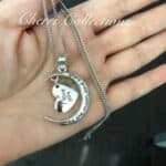 A hand holding a necklace with a heart and a moon on it.