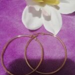 A pair of gold hoop earrings next to a flower.