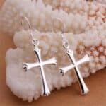 A pair of silver cross earrings sitting on a rock.