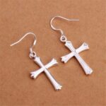 A pair of silver cross earrings on a brown surface.