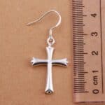 A silver cross shaped earring on top of a ruler.