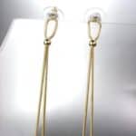 A pair of gold dangling earrings on a stand.