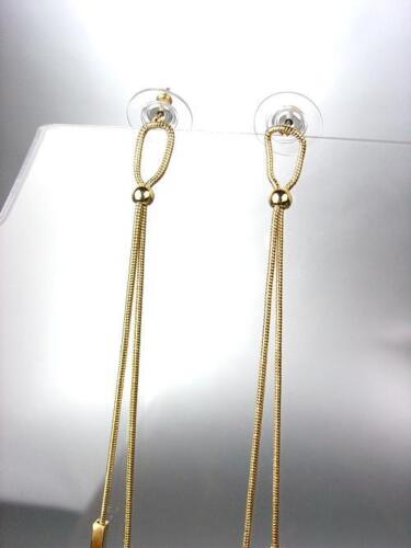 A pair of gold dangling earrings on a stand.