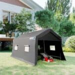 A black tent on a lawn with a lawn mower in it.