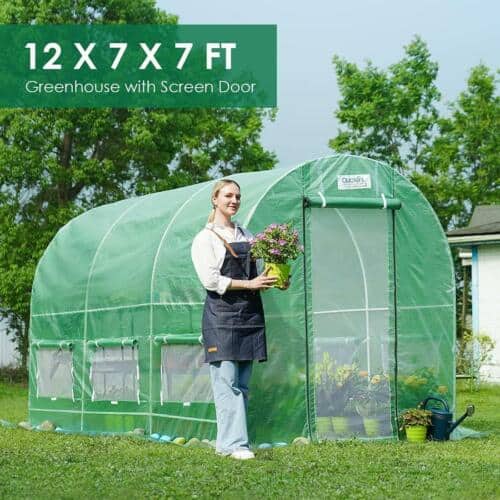 A woman is standing in front of a green greenhouse.