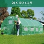 A woman is standing in front of a green greenhouse.