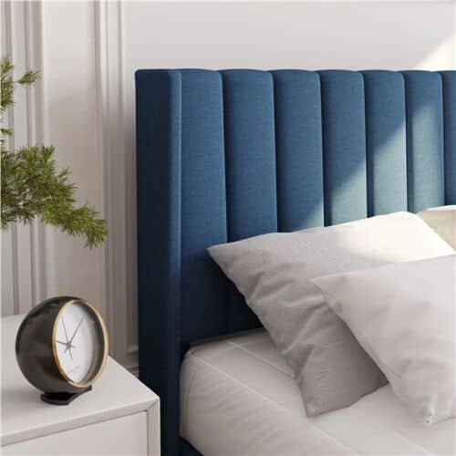 A bed with a blue headboard and a clock next to it.
